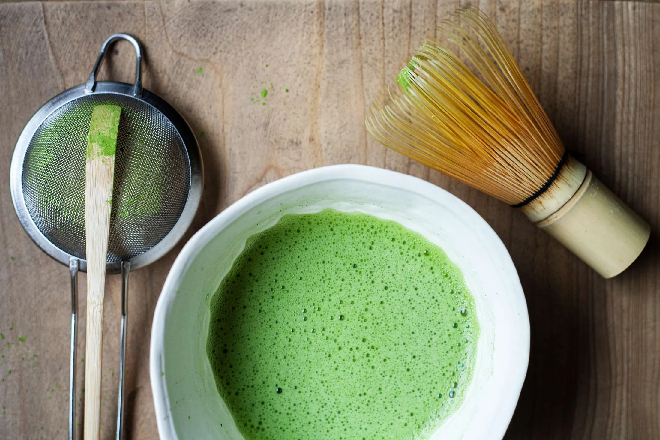 Matcha dentro de uma tigela (chawan), do lado, os utensilios de preparo de matcha como chasen, chashaku e peneira